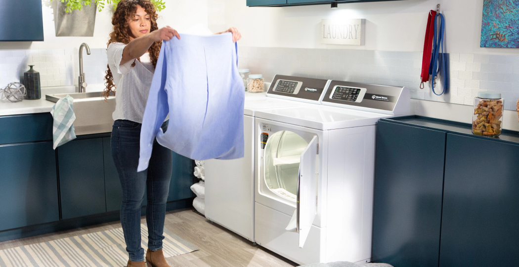 a photo of a woman shaking out laundry in her laundry room next to a washer and dryer